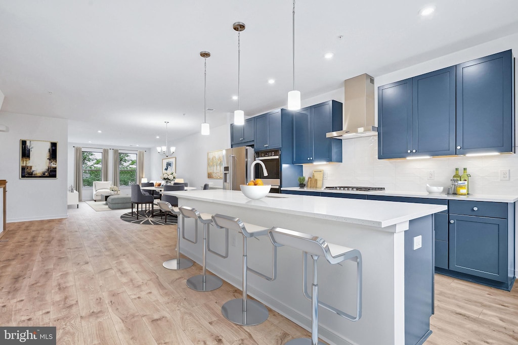 kitchen featuring wall chimney exhaust hood, a kitchen island with sink, and light hardwood / wood-style flooring