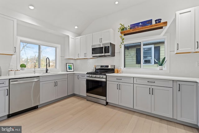 kitchen featuring sink, vaulted ceiling, light wood-type flooring, appliances with stainless steel finishes, and gray cabinets