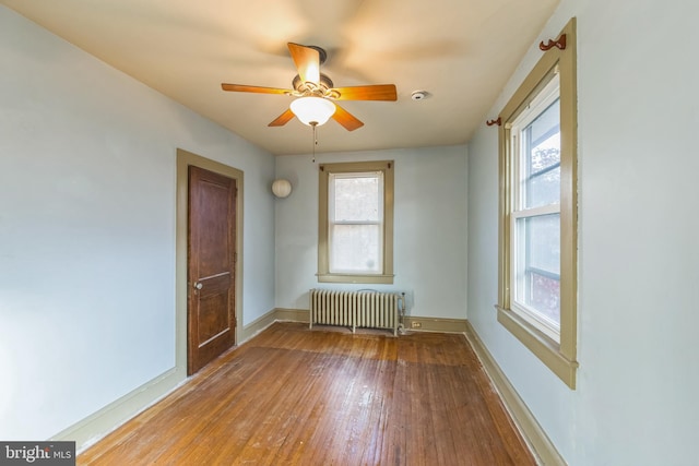 empty room with a wealth of natural light, radiator heating unit, ceiling fan, and wood-type flooring