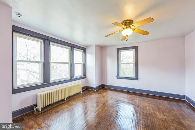 empty room with dark wood-type flooring, ceiling fan, radiator heating unit, and a healthy amount of sunlight