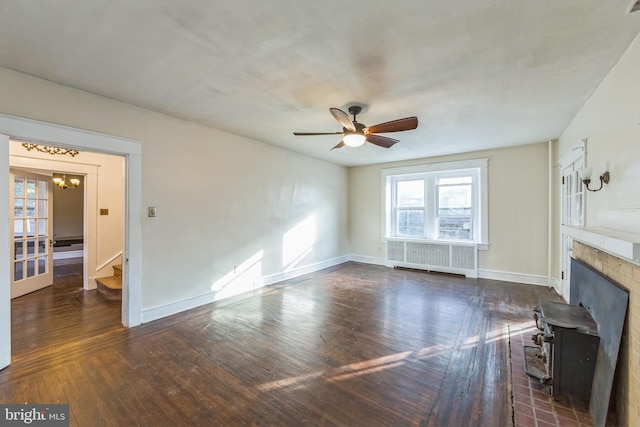 unfurnished living room with ceiling fan with notable chandelier, a wood stove, dark wood-type flooring, and radiator