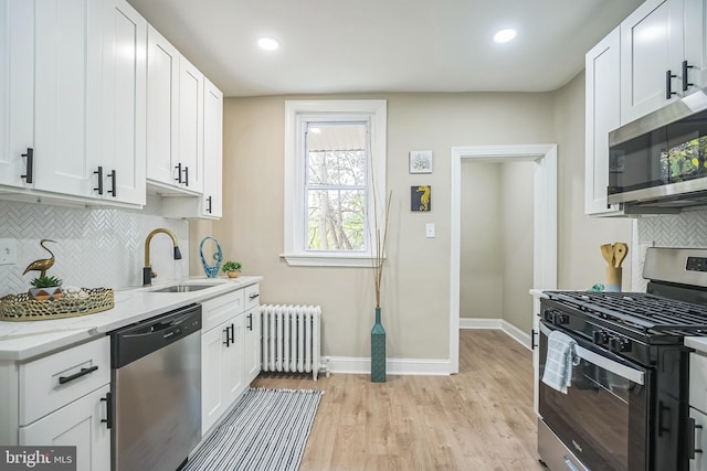 kitchen with white cabinetry, sink, radiator heating unit, and stainless steel appliances