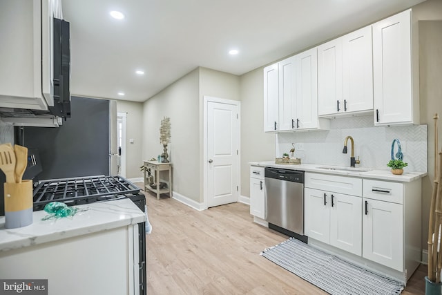 kitchen with light stone countertops, light wood-type flooring, stainless steel dishwasher, sink, and white cabinets