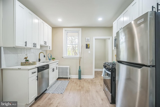 kitchen with radiator, white cabinets, sink, light wood-type flooring, and stainless steel appliances