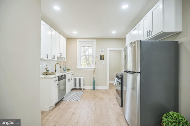 kitchen with appliances with stainless steel finishes, radiator, sink, light hardwood / wood-style floors, and white cabinetry