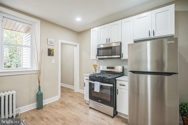 kitchen with radiator, white cabinets, stainless steel appliances, and light hardwood / wood-style floors