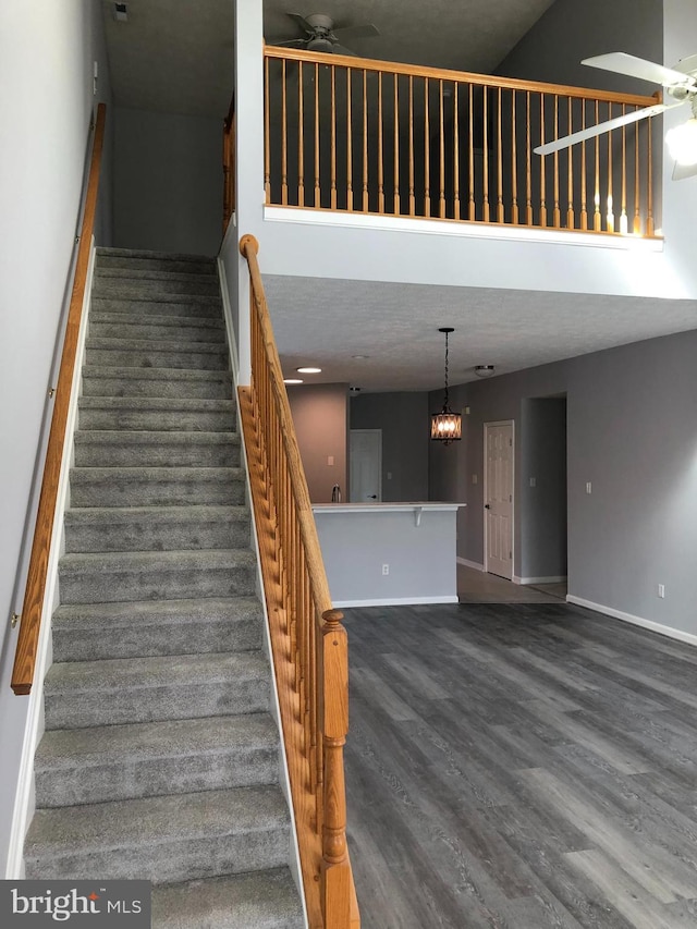 staircase featuring wood-type flooring, ceiling fan, and a high ceiling