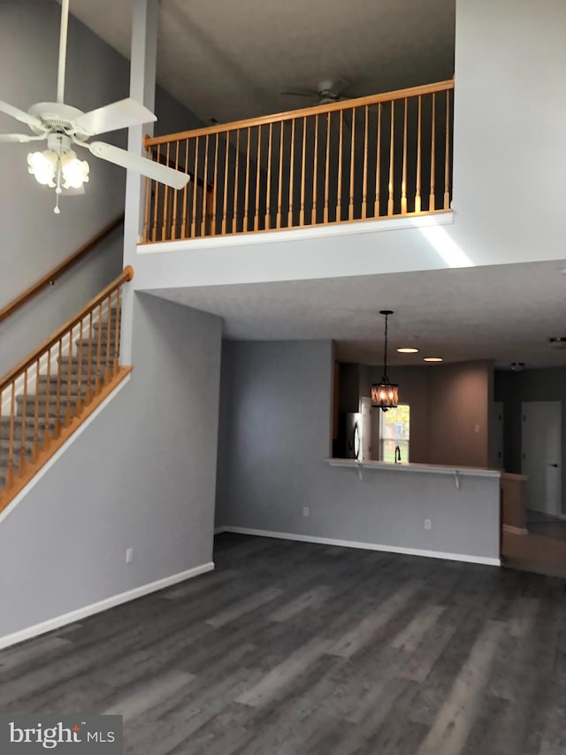 unfurnished living room with dark hardwood / wood-style flooring, high vaulted ceiling, and ceiling fan with notable chandelier