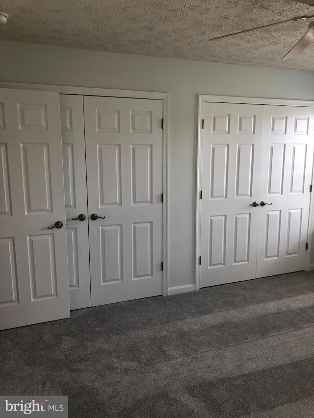 unfurnished bedroom with dark colored carpet, ceiling fan, a textured ceiling, and two closets