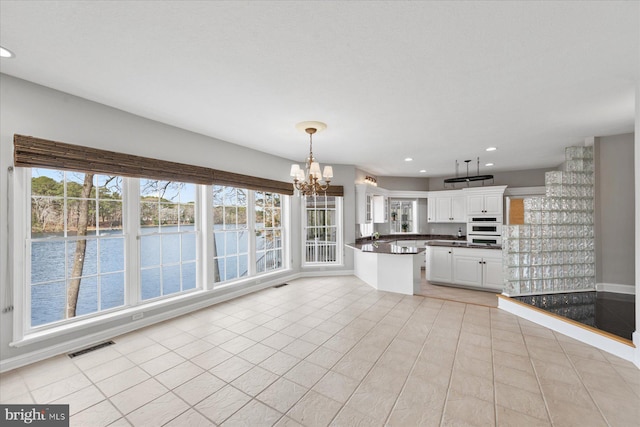 kitchen with a water view, white double oven, dark countertops, white cabinets, and a notable chandelier