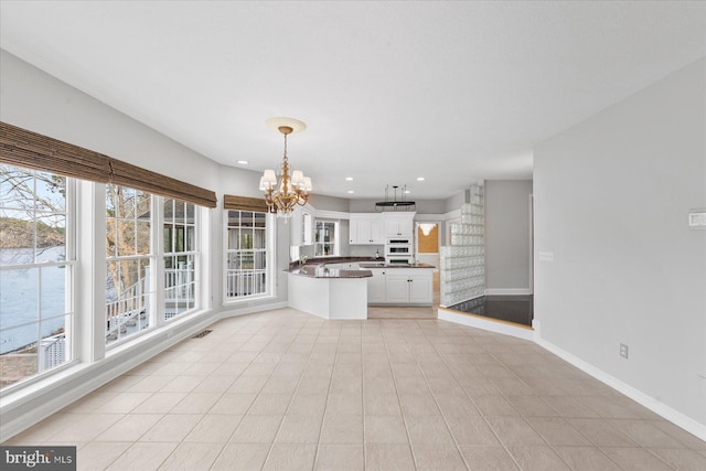 interior space with a notable chandelier, hanging light fixtures, baseboards, dark countertops, and white cabinets