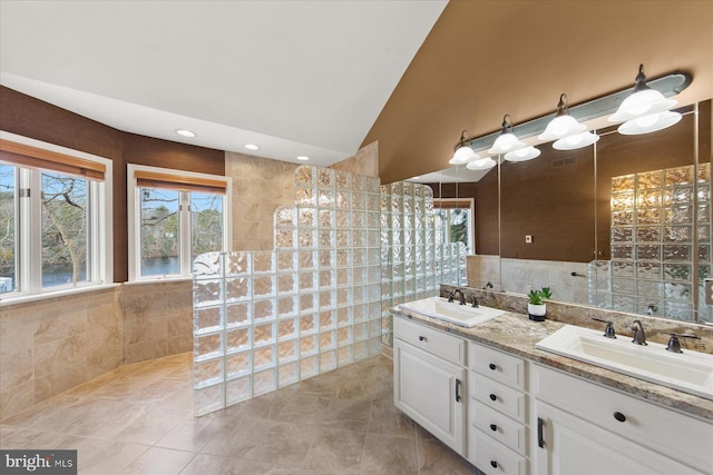 bathroom featuring tile walls, lofted ceiling, a sink, and walk in shower