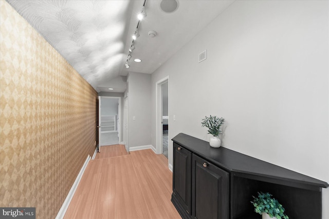 corridor with baseboards, wallpapered walls, visible vents, light wood-style flooring, and track lighting