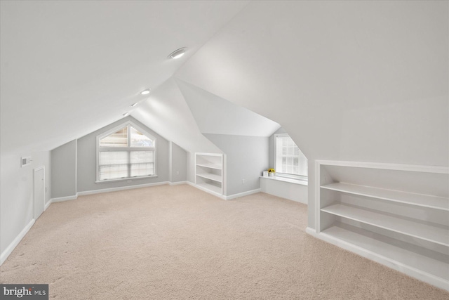 additional living space featuring carpet floors, vaulted ceiling, plenty of natural light, and built in features