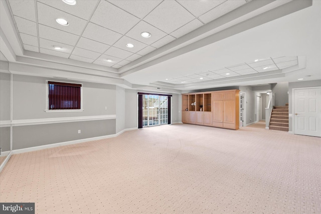 unfurnished living room featuring light carpet, baseboards, stairway, and a raised ceiling