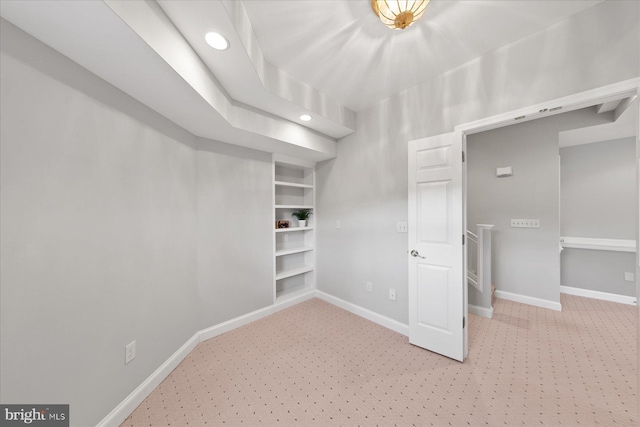 spare room featuring light carpet, built in features, and baseboards