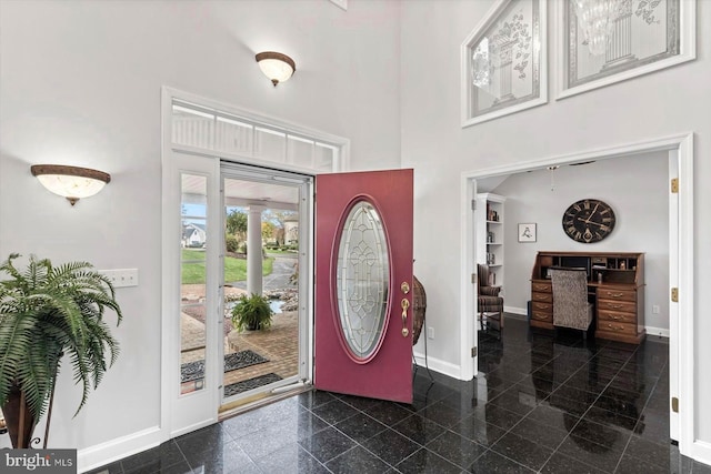 entryway featuring baseboards, granite finish floor, and a high ceiling