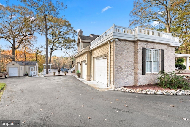 view of side of property featuring a balcony, aphalt driveway, a chimney, a garage, and brick siding