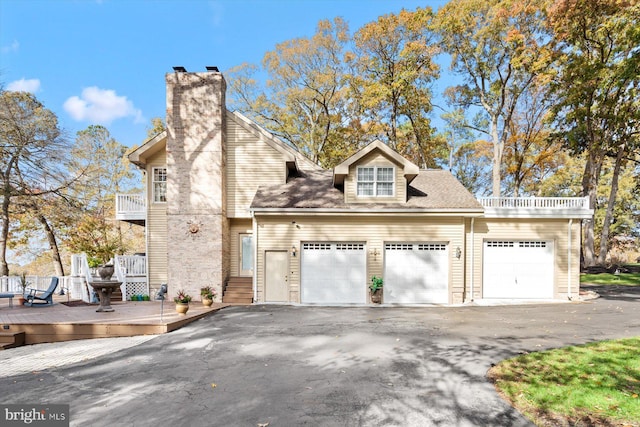 view of front of property featuring a balcony, aphalt driveway, a wooden deck, an attached garage, and a chimney