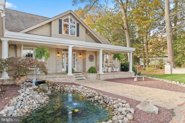 view of front facade featuring a shingled roof, covered porch, and brick siding