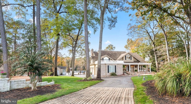 view of front of home with a balcony, decorative driveway, a chimney, a front yard, and a porch