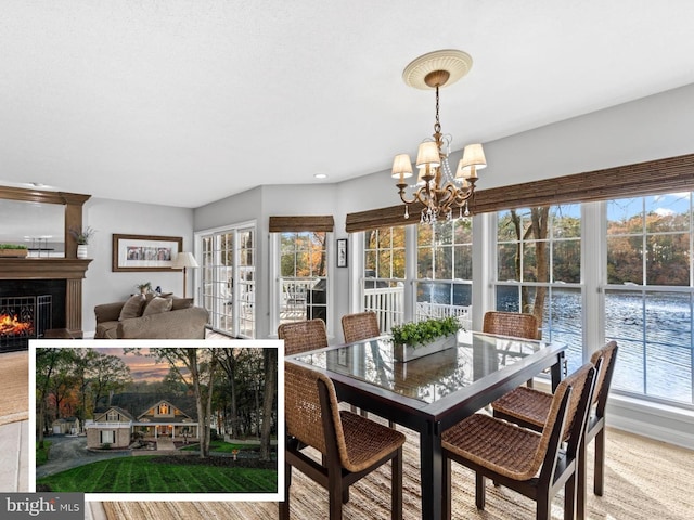 dining area with a notable chandelier, a water view, and a lit fireplace
