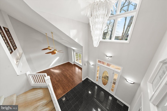 foyer entrance with a towering ceiling, wood finished floors, baseboards, visible vents, and ceiling fan