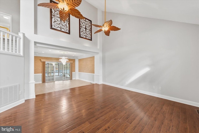 unfurnished living room with visible vents, baseboards, a towering ceiling, ceiling fan with notable chandelier, and wood-type flooring