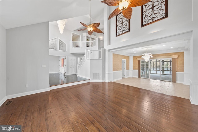 unfurnished living room featuring hardwood / wood-style floors, high vaulted ceiling, ceiling fan with notable chandelier, and visible vents