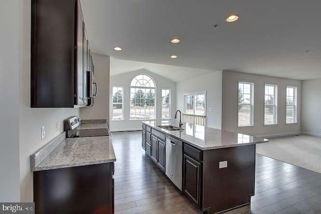 kitchen with light stone counters, an island with sink, stainless steel appliances, dark brown cabinetry, and sink