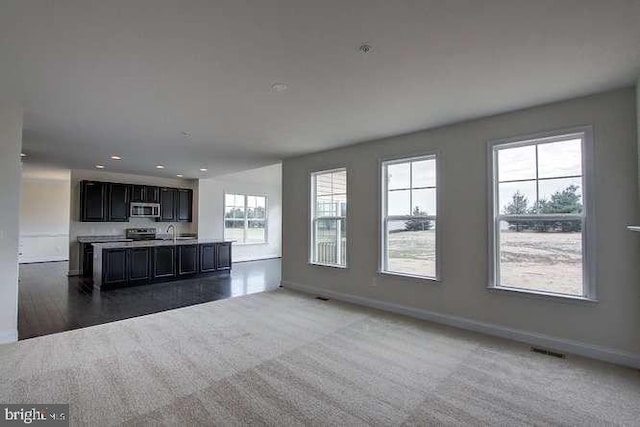 unfurnished living room with sink, dark carpet, and plenty of natural light