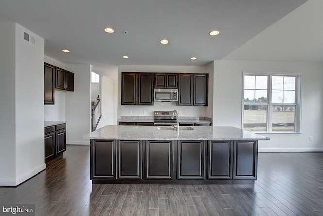 kitchen featuring stainless steel appliances, sink, light stone countertops, a kitchen island with sink, and dark wood-type flooring