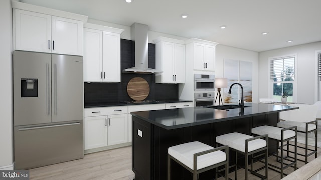 kitchen with a center island with sink, white cabinets, sink, wall chimney exhaust hood, and appliances with stainless steel finishes