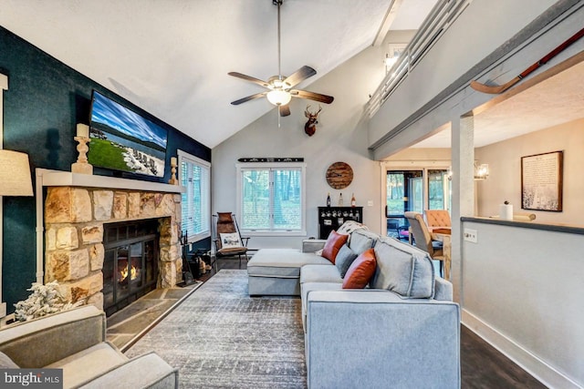 living room with a stone fireplace, ceiling fan, plenty of natural light, and dark wood-type flooring