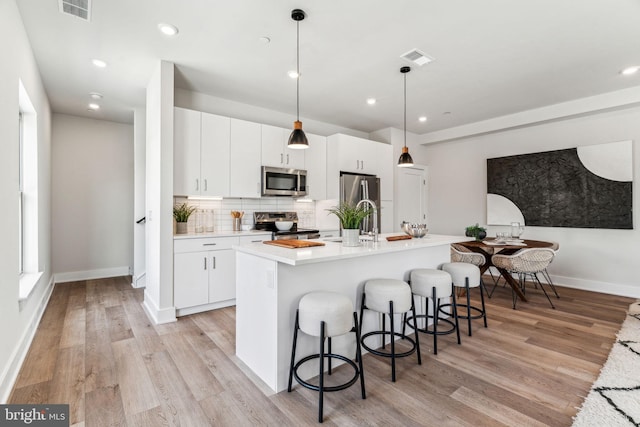 kitchen featuring a kitchen bar, hanging light fixtures, stainless steel appliances, a kitchen island with sink, and white cabinets