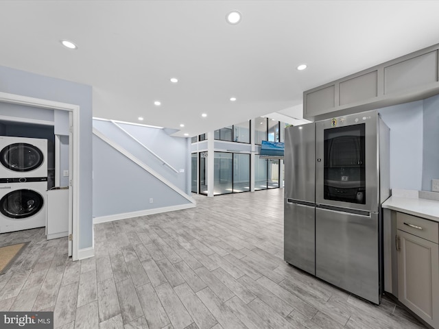 kitchen with gray cabinets, stainless steel fridge, stacked washing maching and dryer, and light hardwood / wood-style floors