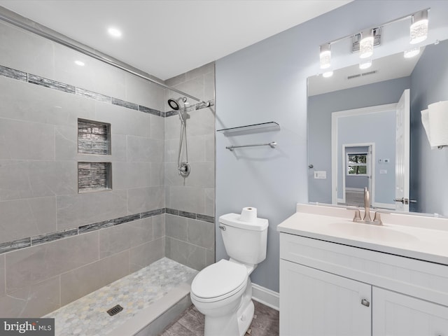 bathroom with a tile shower, vanity, and toilet