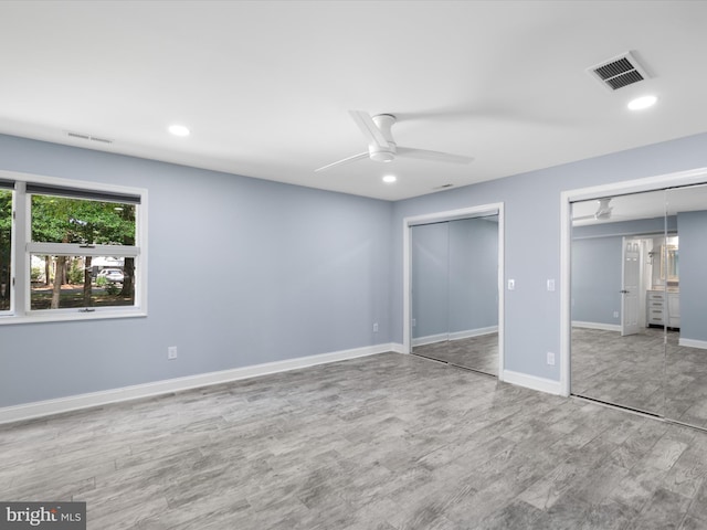 unfurnished bedroom with ceiling fan, wood-type flooring, and two closets