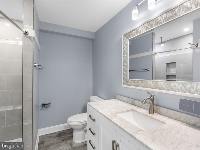 bathroom with hardwood / wood-style floors, vanity, toilet, and tiled shower