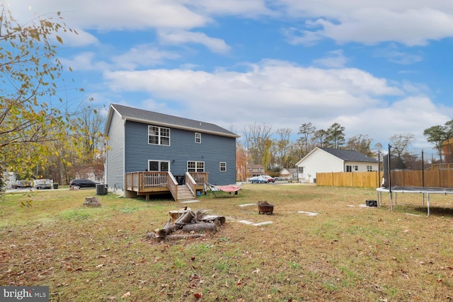 rear view of property featuring a wooden deck, central AC, a fire pit, and a trampoline