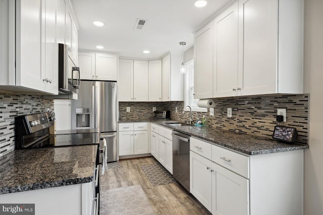 kitchen with stainless steel appliances, white cabinetry, hanging light fixtures, and light hardwood / wood-style flooring