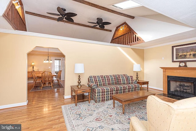 living room with ornamental molding, lofted ceiling with beams, ceiling fan with notable chandelier, and light wood-type flooring