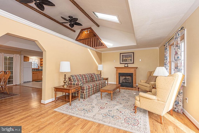 living room featuring ceiling fan, crown molding, lofted ceiling with skylight, light hardwood / wood-style floors, and a fireplace