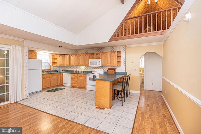 kitchen with white appliances, high vaulted ceiling, light hardwood / wood-style floors, a kitchen bar, and kitchen peninsula