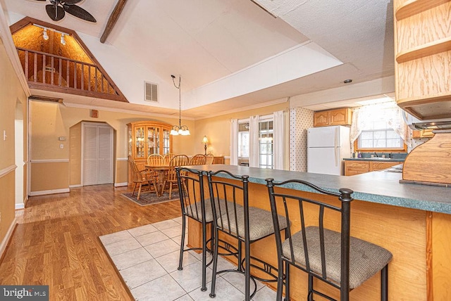 kitchen with ceiling fan with notable chandelier, light wood-type flooring, white fridge, and a breakfast bar area