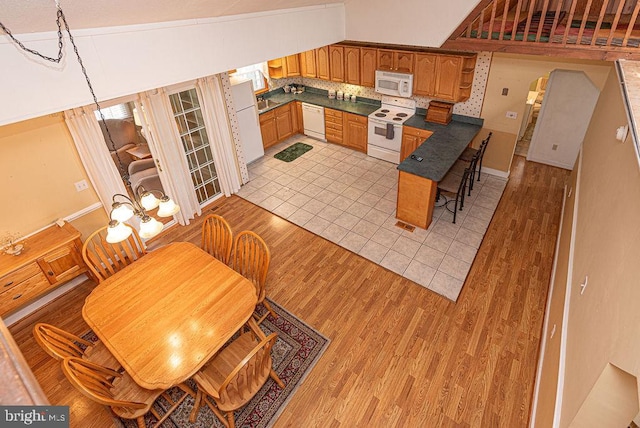 kitchen with a notable chandelier, vaulted ceiling, white appliances, and light hardwood / wood-style flooring