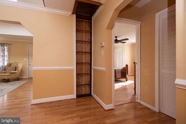 hallway with crown molding, built in features, and light hardwood / wood-style floors