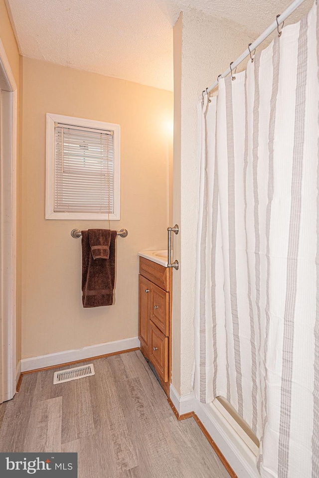 bathroom featuring vanity, wood-type flooring, a textured ceiling, and walk in shower