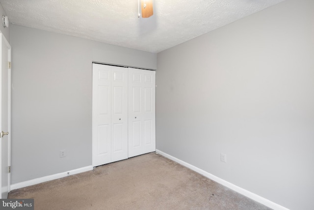 unfurnished bedroom with ceiling fan, light colored carpet, a textured ceiling, and a closet