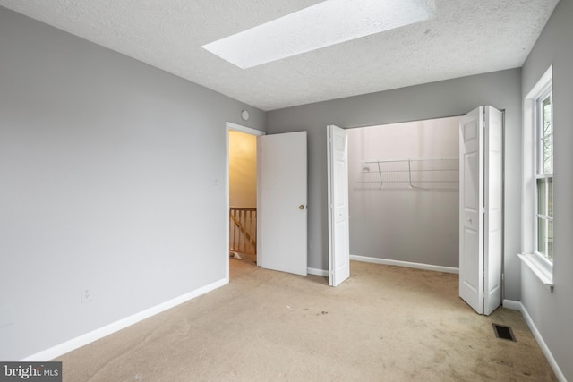 unfurnished bedroom with a closet, light colored carpet, a textured ceiling, and a skylight